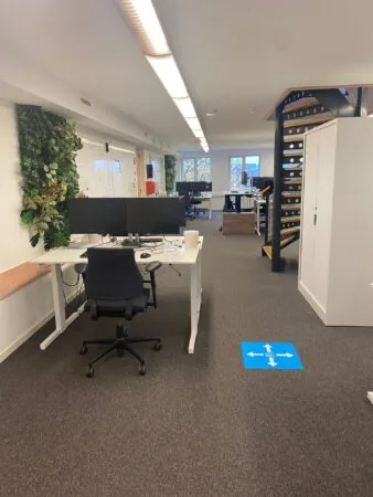 Modern kantoorinterieur aan de Prins Hendrikkade met bureaus, computers, een wenteltrap en muurdecoratie van planten.